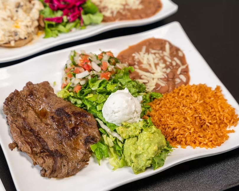 Grilled steak with rice, refried beans, guacamole, sour cream, and a side salad.