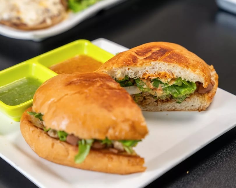 Two halves of a sandwich with lettuce, meat, and sauce, served with two dipping sauces.