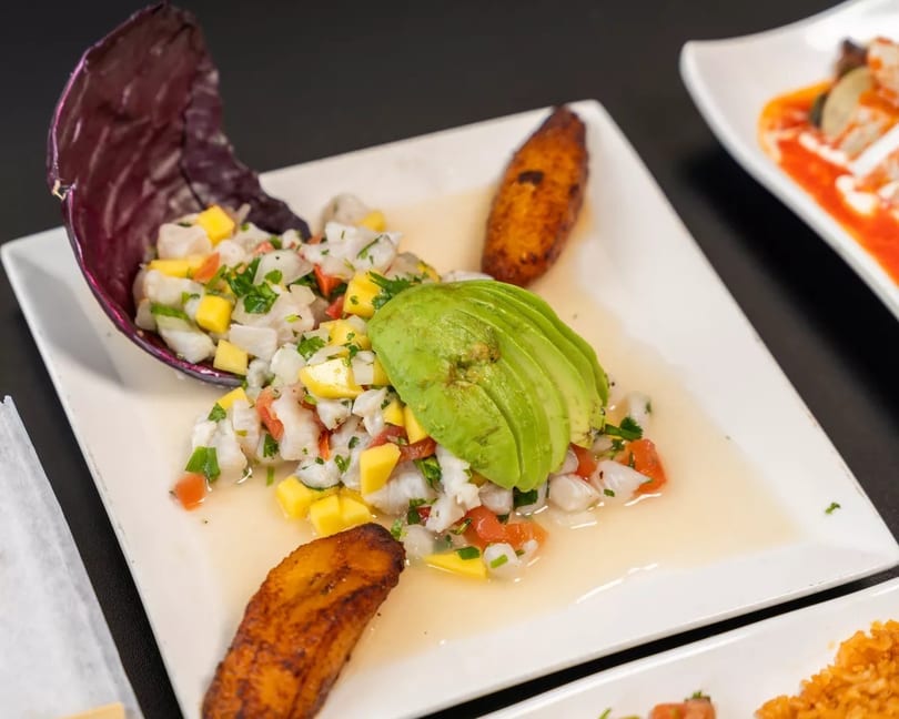 Ceviche with mango, avocado, and plantains on a white plate.