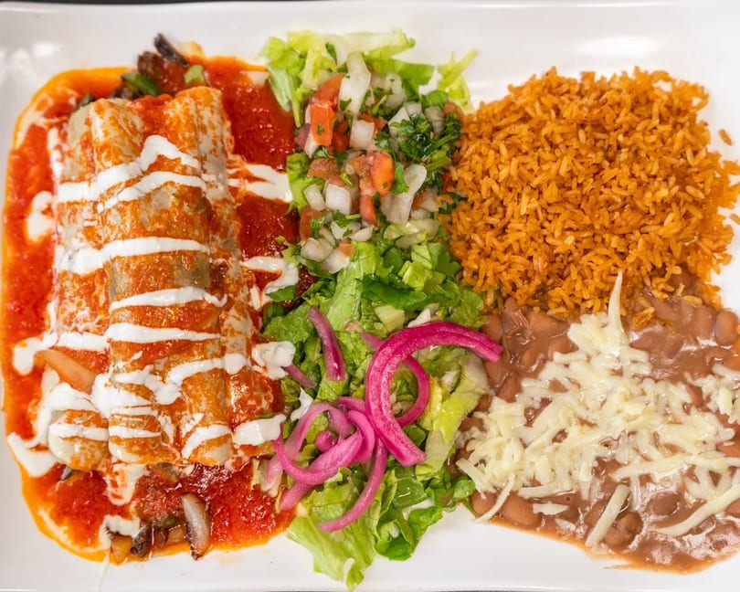 Enchiladas with red sauce and crema, served with rice, refried beans, and a side salad.