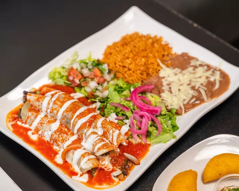 A plate of enchiladas with red sauce, crema, rice, beans, and a side salad.